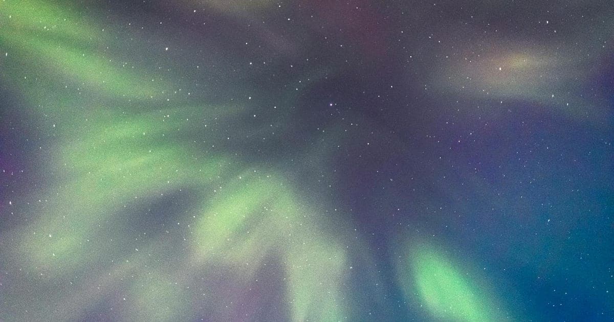 Vivid green and purple northern lights dancing over a snowy Arctic landscape with a frozen lake in the foreground