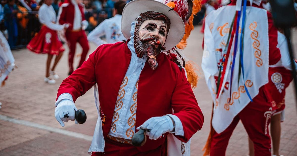 A masked dancer in a red embroidered costume during a carnival parade