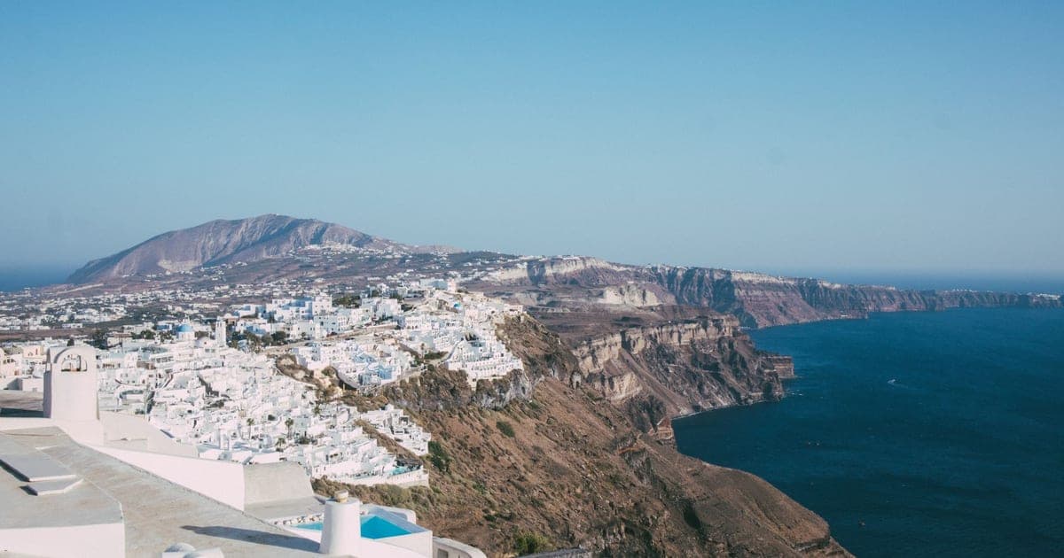 Case imbiancate a calce sopra la caldera di Santorini al crepuscolo con un traghetto che attraversa l'Egeo in basso