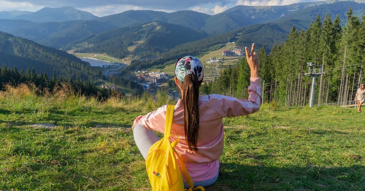 Mulher viajando sozinha com mochila contemplando uma paisagem costeira ao entardecer