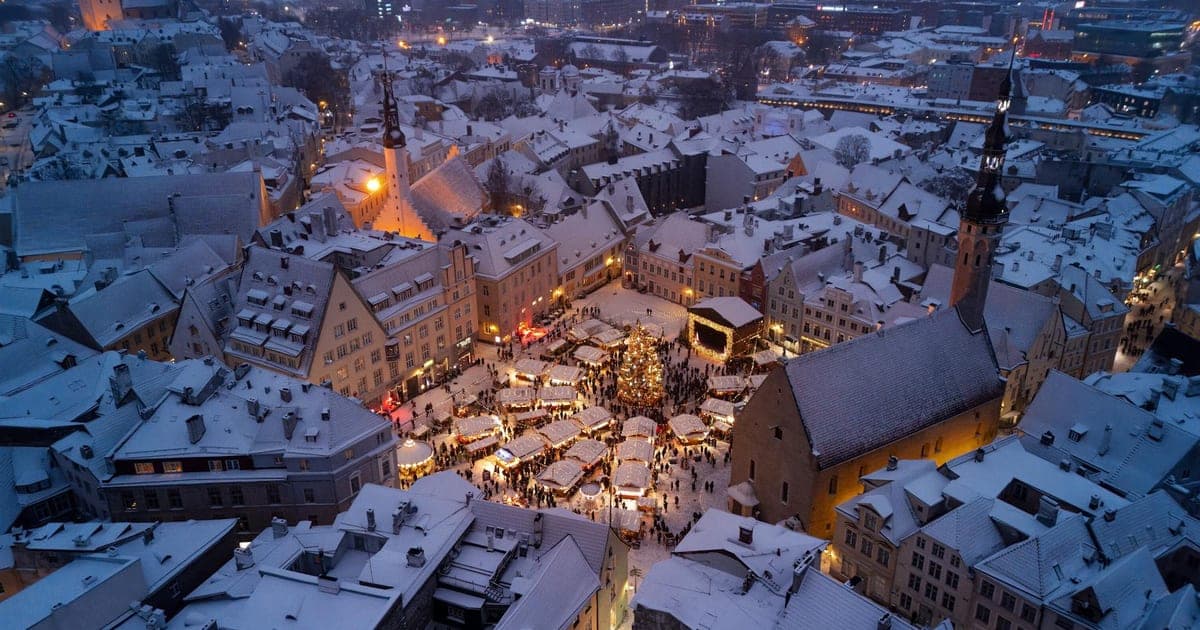 Glowing Christmas market stalls in a snow-dusted European old town square at dusk in December