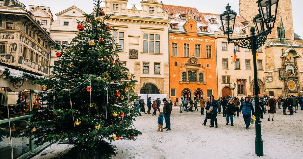 Un albero di Natale addobbato sotto una leggera nevicata in Piazza della Città Vecchia a Praga, con l'orologio astronomico sulla destra