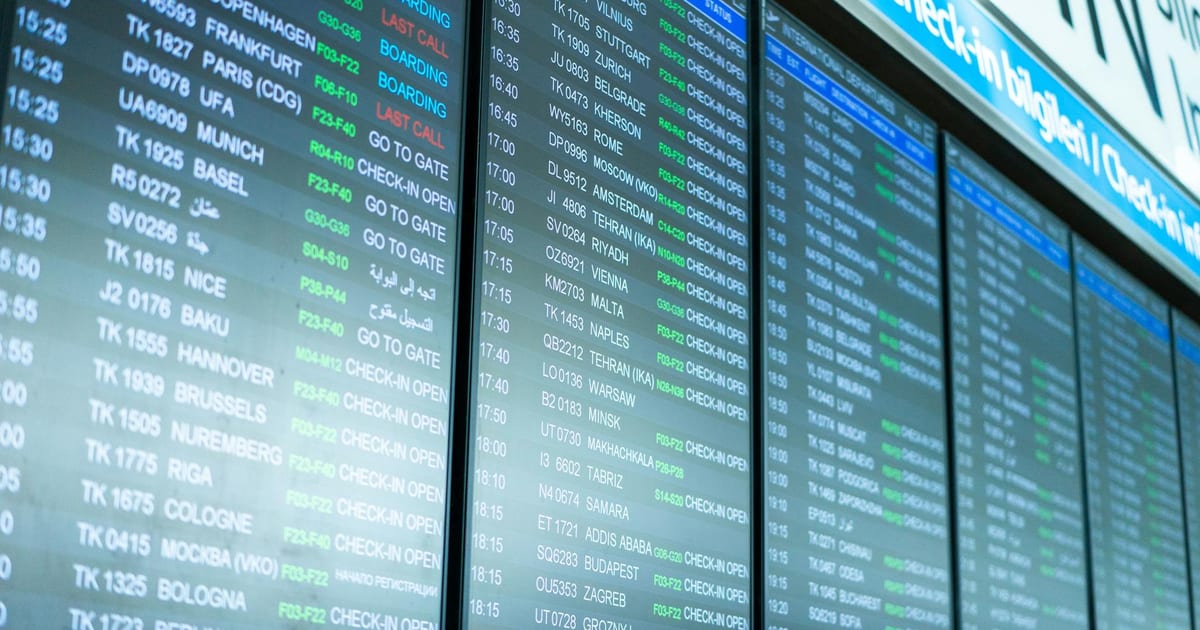 Airport departure board showing flight prices with a traveler checking their phone