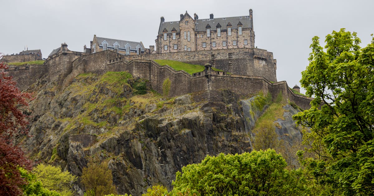Il Castello di Edimburgo illuminato di notte durante il Festival Fringe con artisti colorati in primo piano
